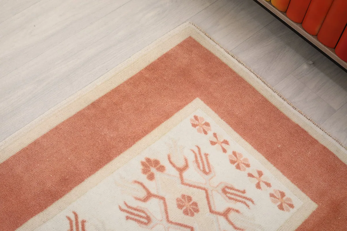 Angled close-up of the corner of the rug, highlighting the orange border and ivory pattern.