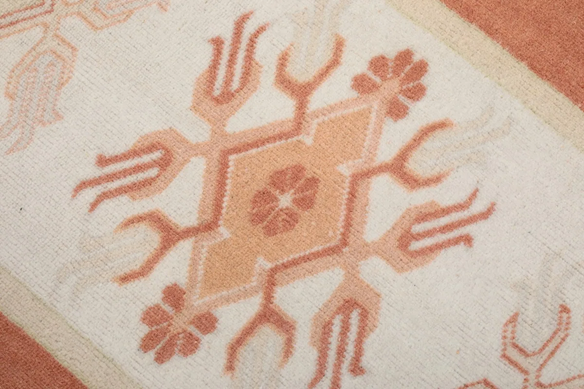 Detailed view of a single central geometric motif in orange and rust on the ivory field.