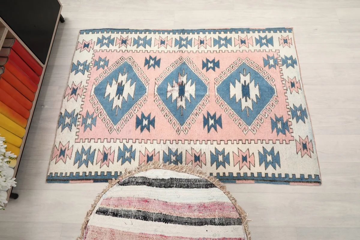 Overhead shot of the entire pink and blue geometric rug on the floor, next to a pouf.