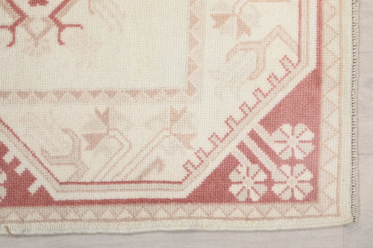 Detailed shot of the rug's corner and border design with rose and cream tones