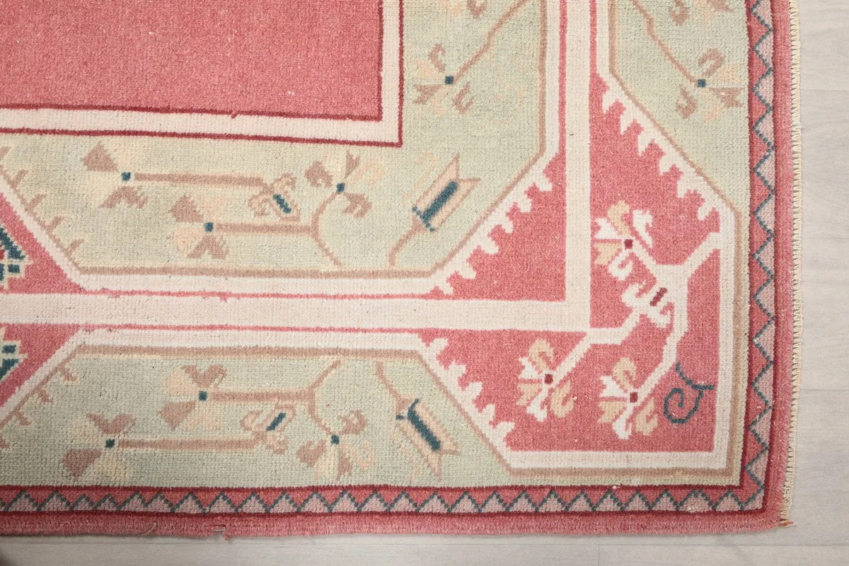 Detailed view of the corner of the rug, highlighting the pink and green geometric and floral patterns.