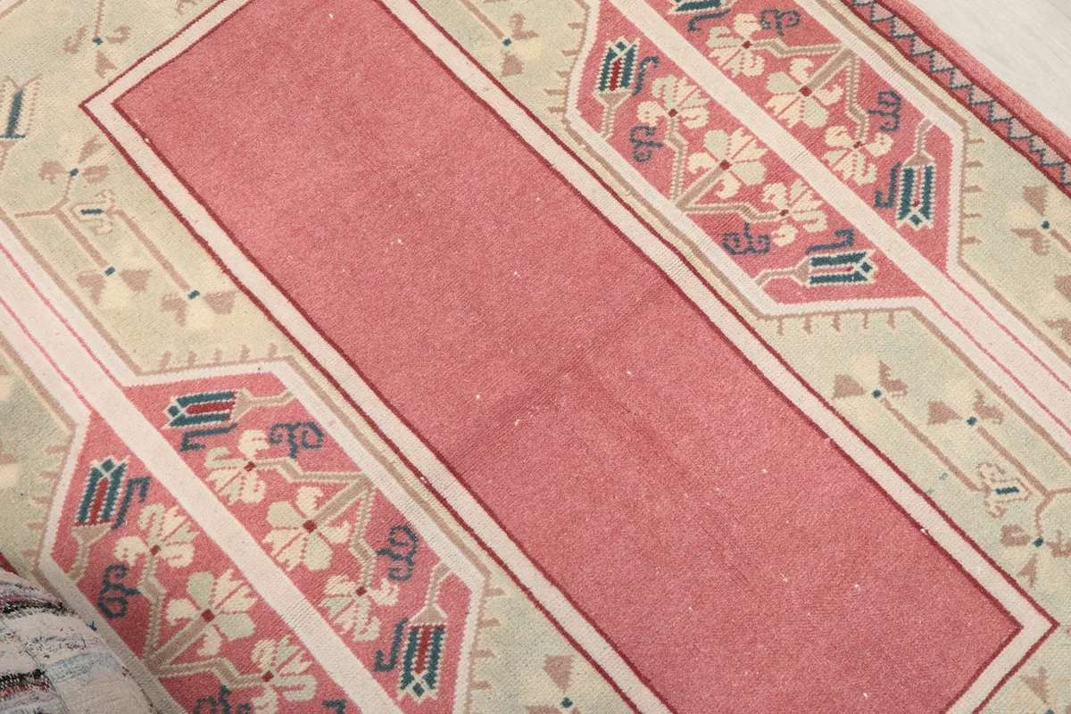 Close-up of the pink central field and patterned green border, showing the rug's texture.
