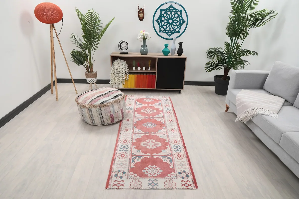 Rose and ivory runner rug laid in a modern living room setting with a light gray sofa and wooden cabinet.