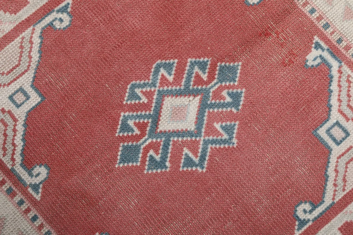 Extreme close-up of a central geometric motif in blue, ivory, and rose, showing the hand-knotted texture.