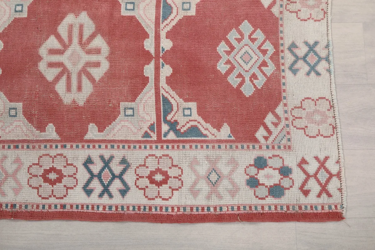 Detailed view of the rug's corner, showcasing the ivory border with floral and geometric motifs against the rose field.