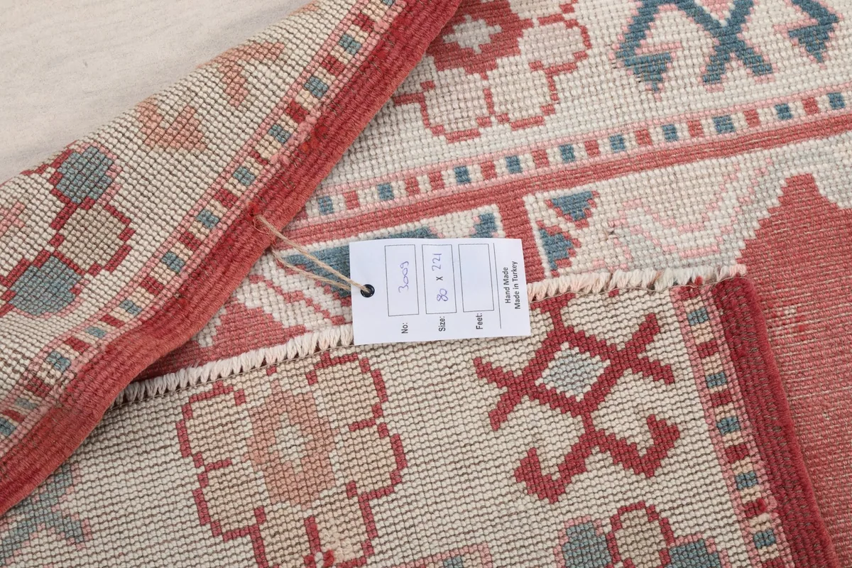Detail of the rug's corner with a product tag, showing the hand-knotted structure and fringe.
