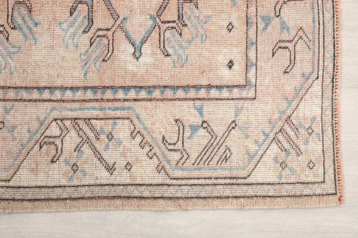 Detailed view of the geometric border and tribal motifs in rose beige and blue