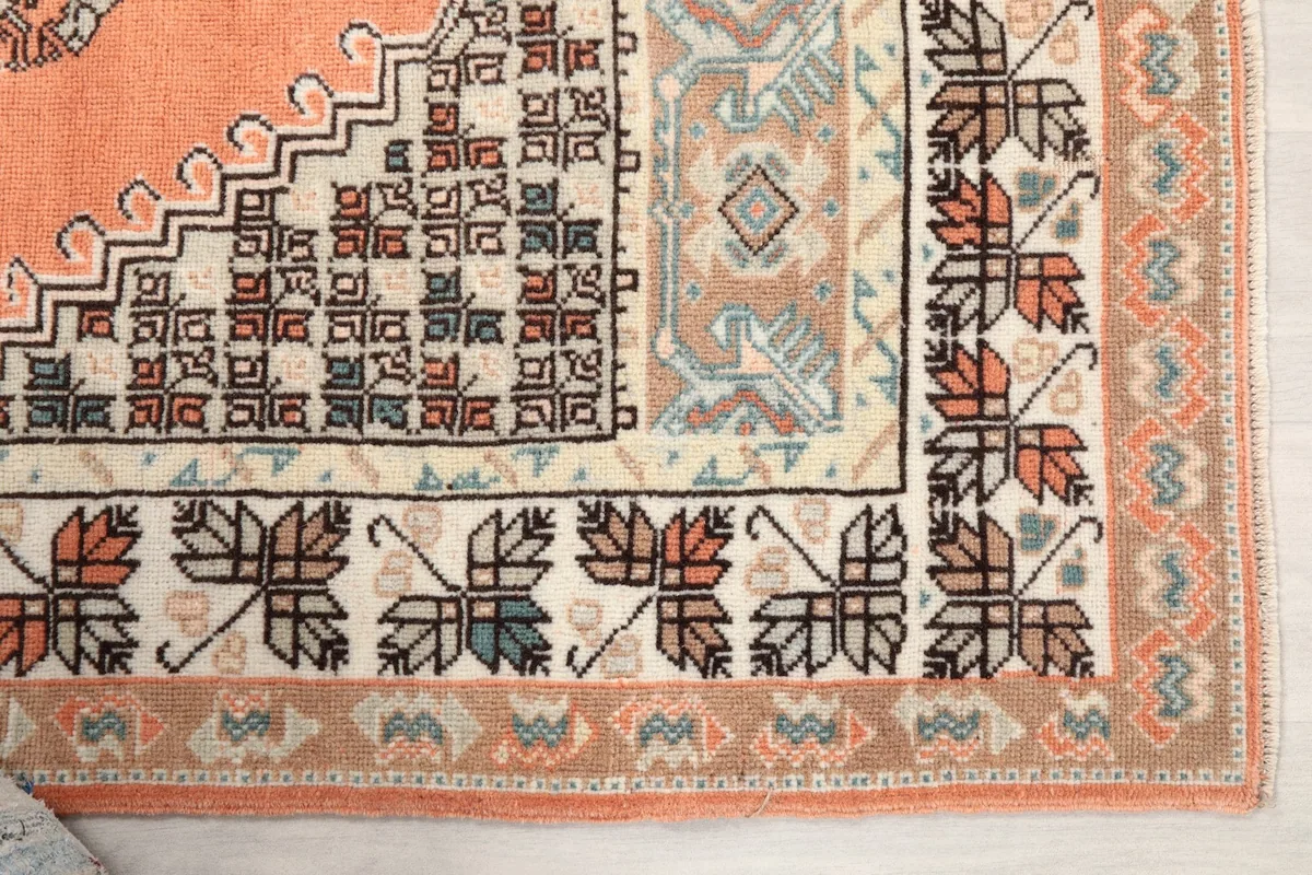 Detailed view of the corner of the rug, highlighting the cream border and tribal motifs