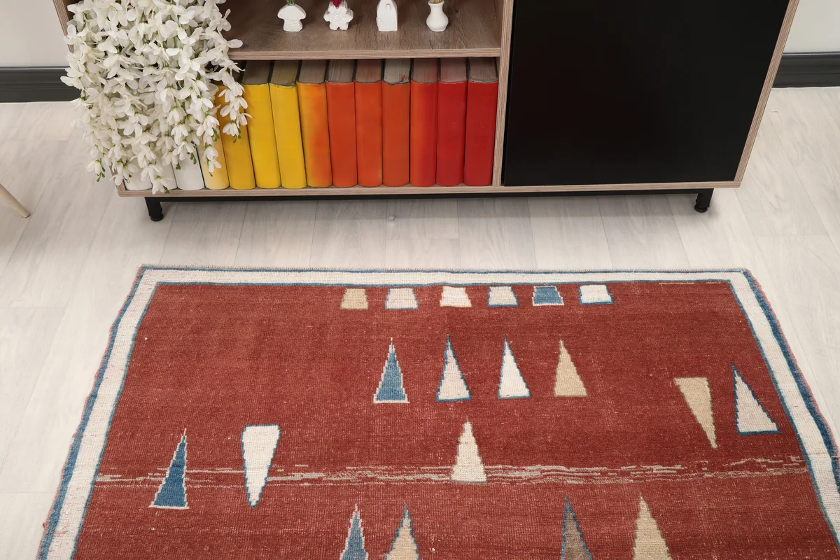 Overhead angled view of the Rust Geometric Anatolian Rug, positioned in front of a colorful bookshelf.