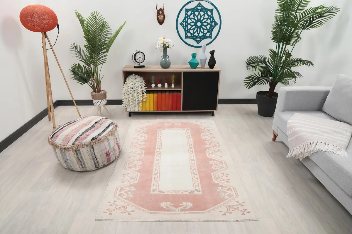 Vintage rose and ivory geometric rug placed in a living room setting with a gray sofa and wooden console.