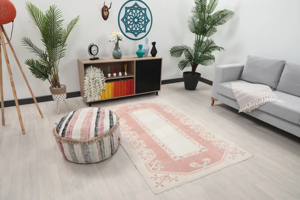 Angled view of the rose and ivory rug in a room, showing its placement near a sofa and a striped pouf.
