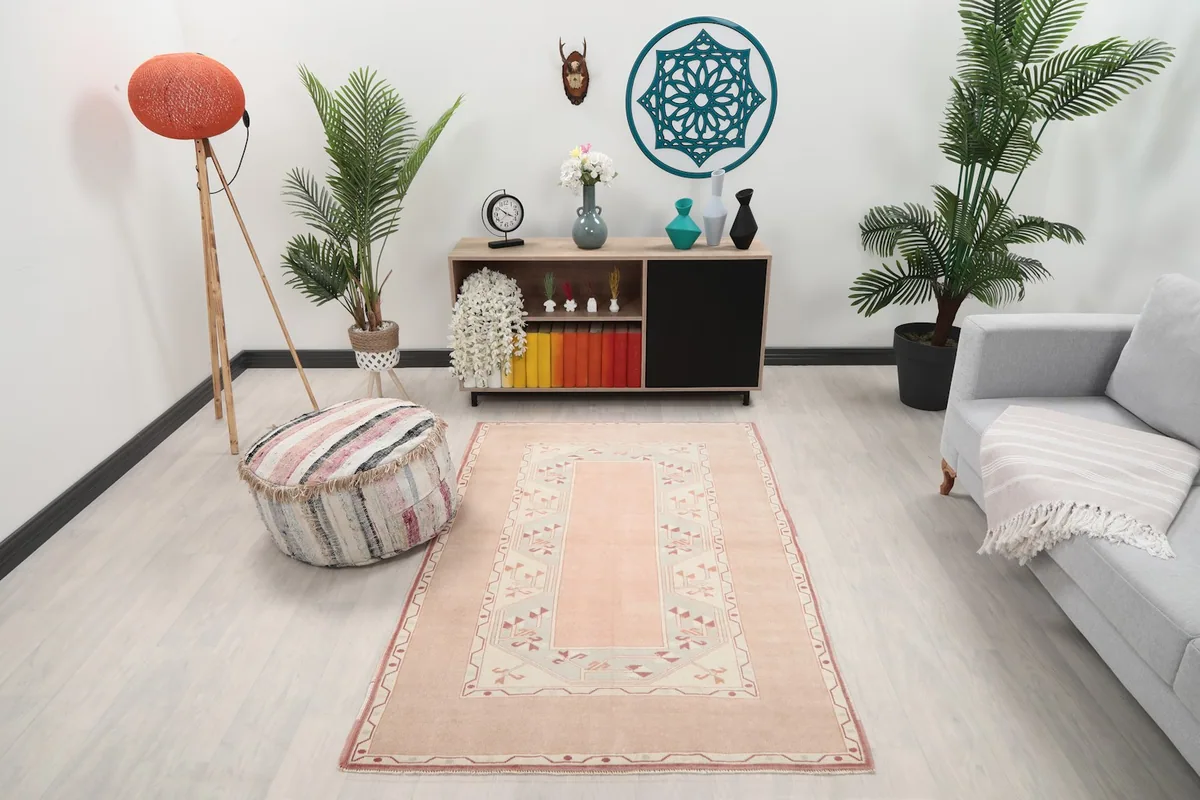 Vintage pink and beige rug placed in a living room setting with a gray sofa and wooden cabinet
