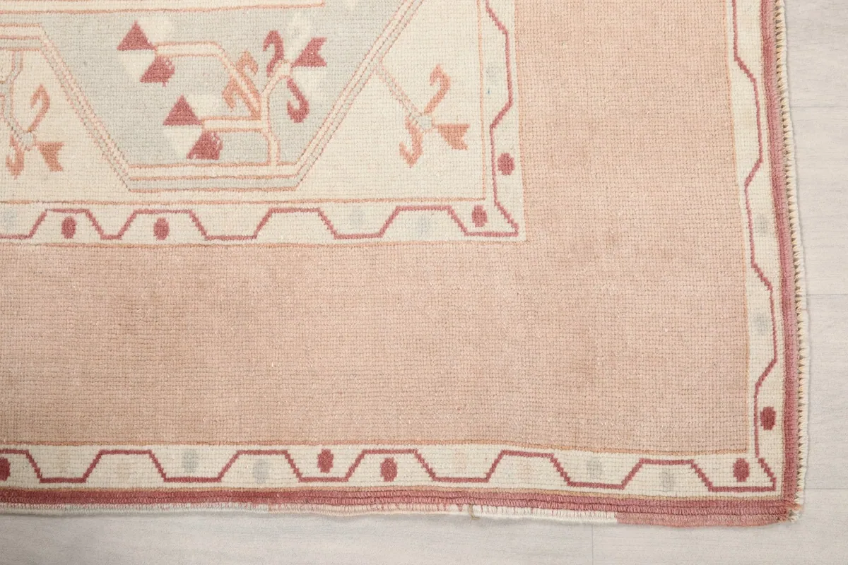 Detailed view of the rug's beige border with red geometric patterns and the pink field