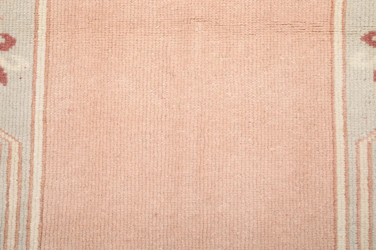 Close-up showing the low wool pile texture and soft pink color of the rug's field