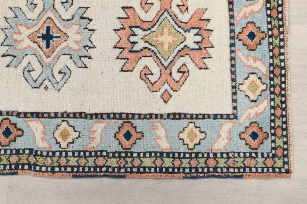 Detailed view of the rug's ivory field, blue border, and geometric motifs