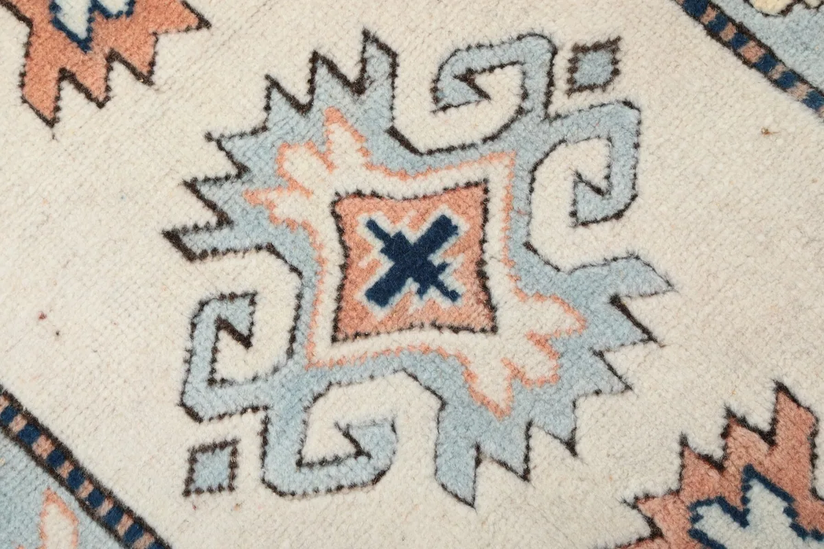Close-up of a central geometric motif in blue, rose, and navy on the ivory field