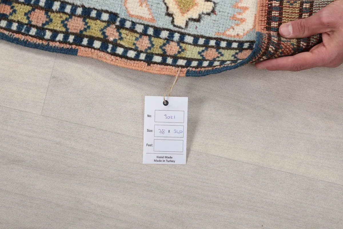 Hand holding a tag with rug details, showing the rug's edge and fringe