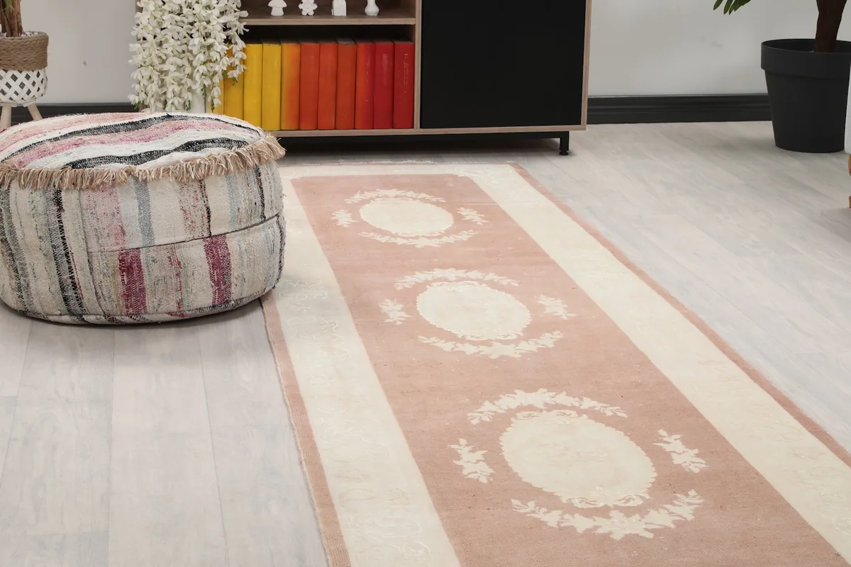 Close-up angle of the rose and ivory runner rug showing a floral medallion and a striped ottoman