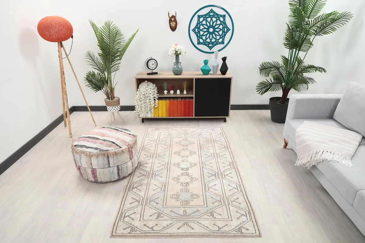 Vintage beige and blue rug placed in a modern living room setting with a sofa and ottoman.