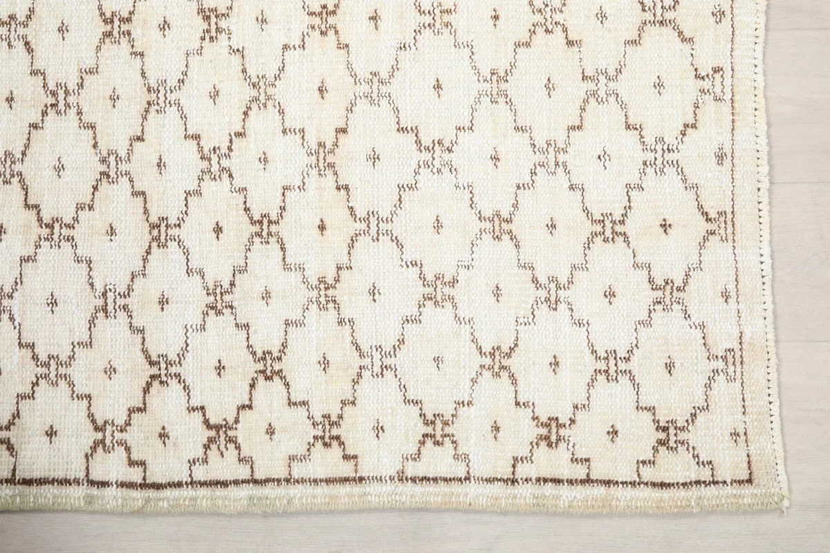 Detailed view of the brown geometric motifs on the cream wool pile of the rug