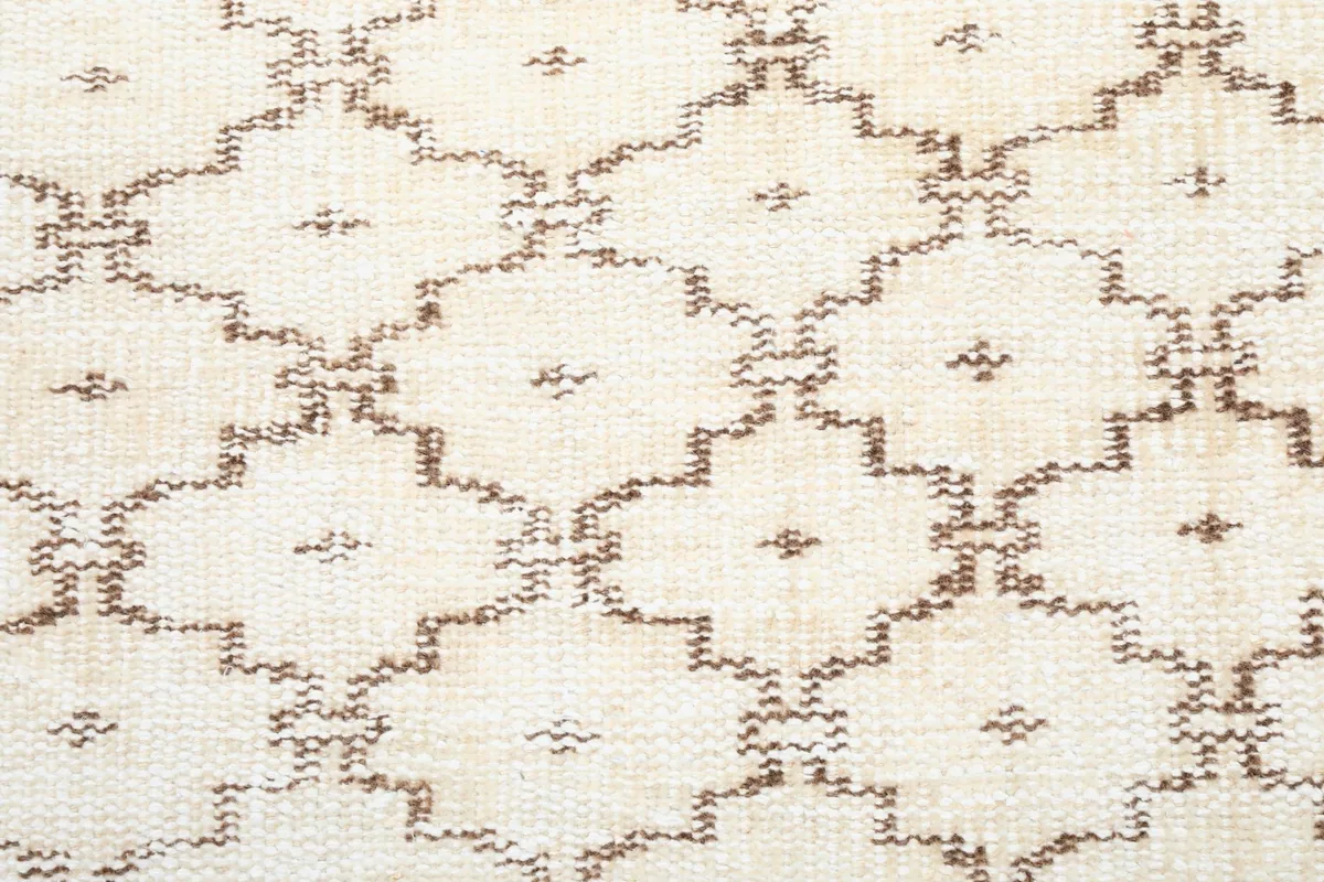 Extreme close-up of the hand-knotted brown geometric pattern against the cream background
