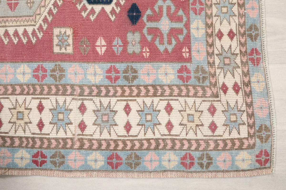 Detailed view of the rug's corner showcasing geometric motifs in blue, rose, and ivory
