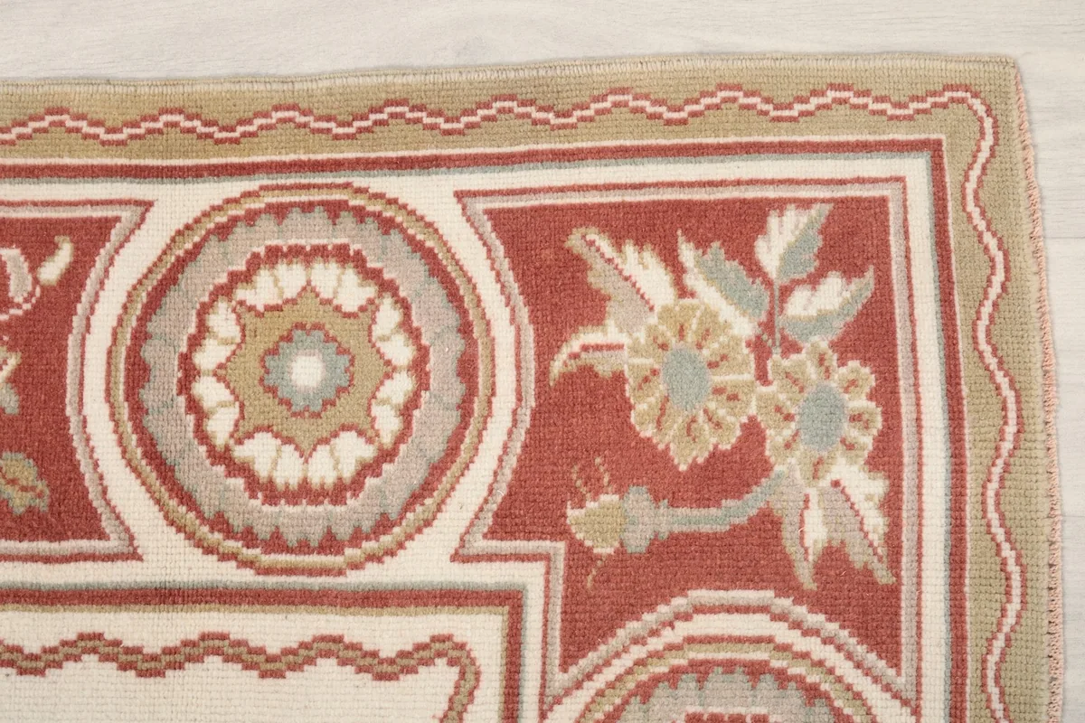 Detailed view of the rust border with floral and circular medallion motifs in tan and gray
