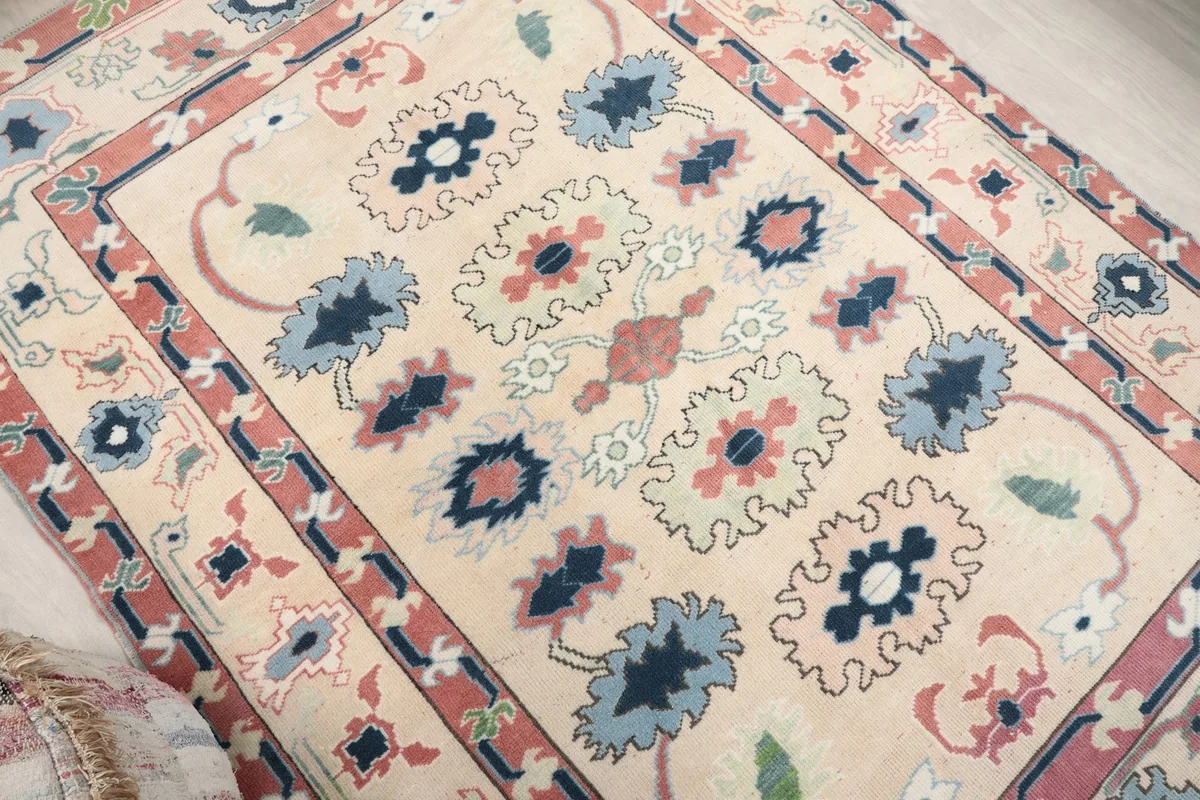 Overhead angle view of the ivory, rose, and blue vintage rug's central floral and geometric patterns.