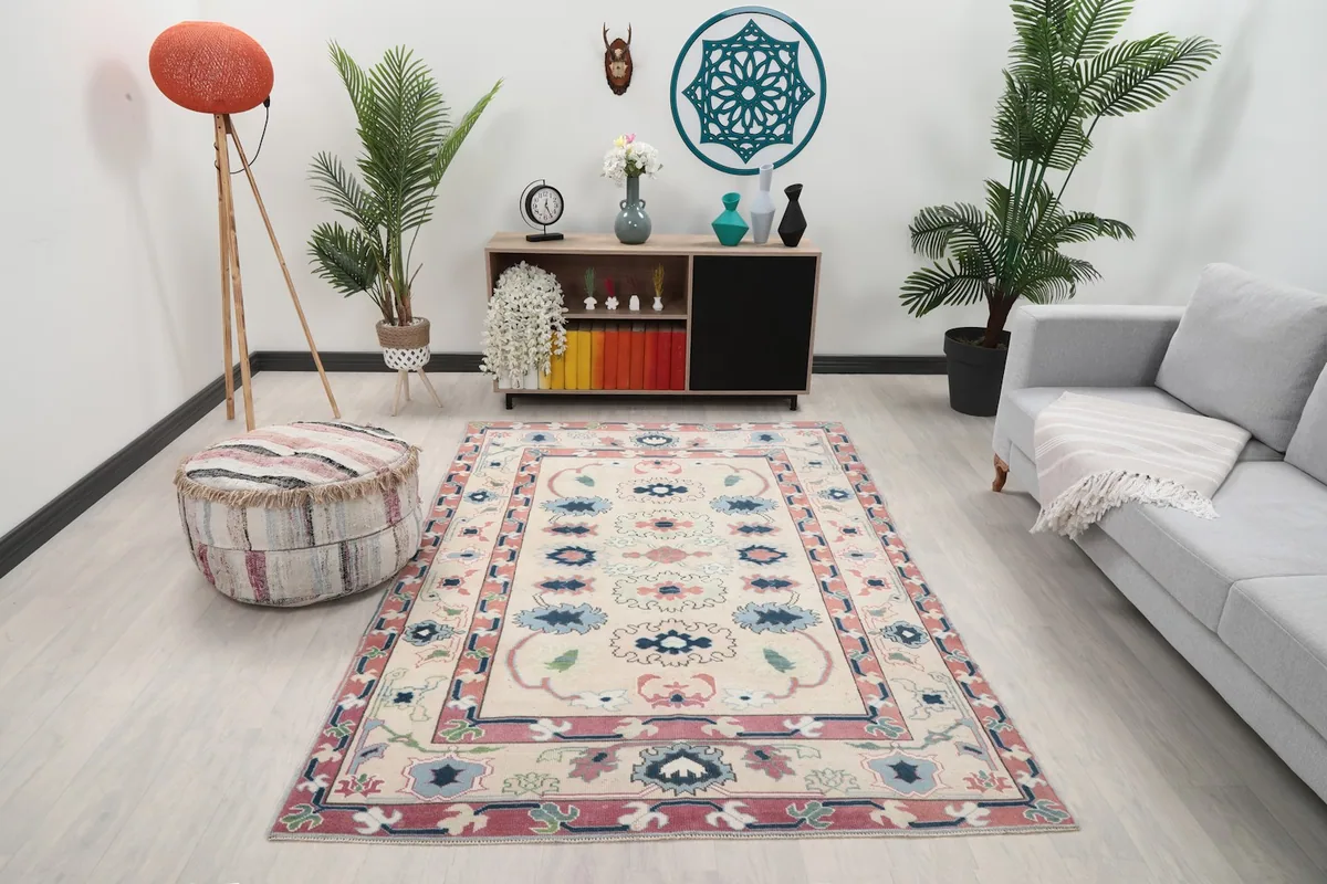 Ivory, rose, and blue vintage Anatolian rug placed in a living room setting with a sofa and ottoman.