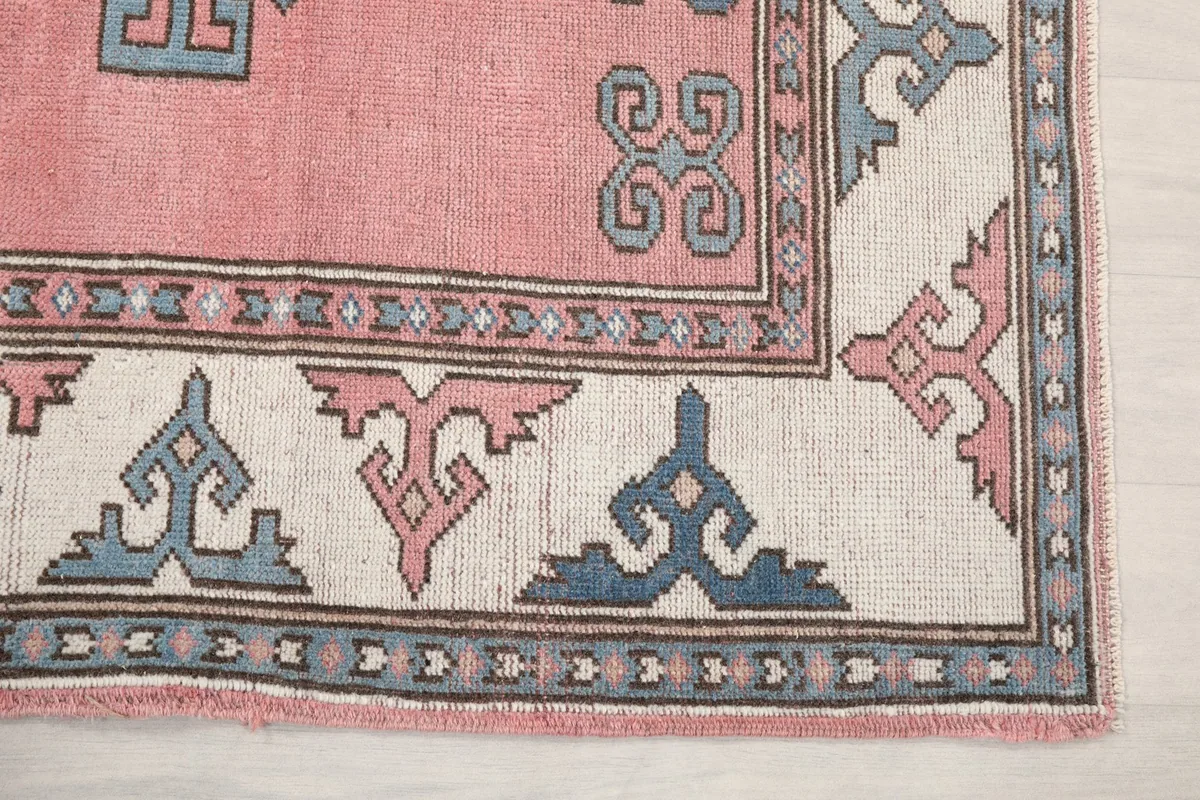 Detail view of the rug's ivory border with blue and pink geometric patterns and corner design
