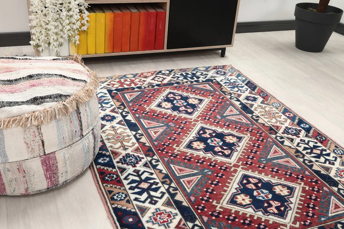 Close-up angle showing the red field and navy geometric patterns of the rug next to an ottoman
