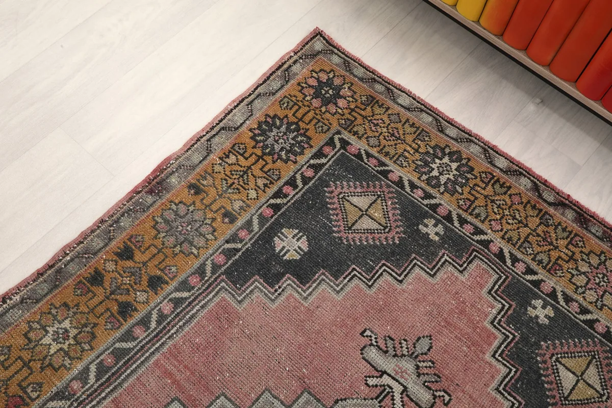 Corner detail of the rug, showing the blend of rose, gold, navy, and gray tones in the motifs.