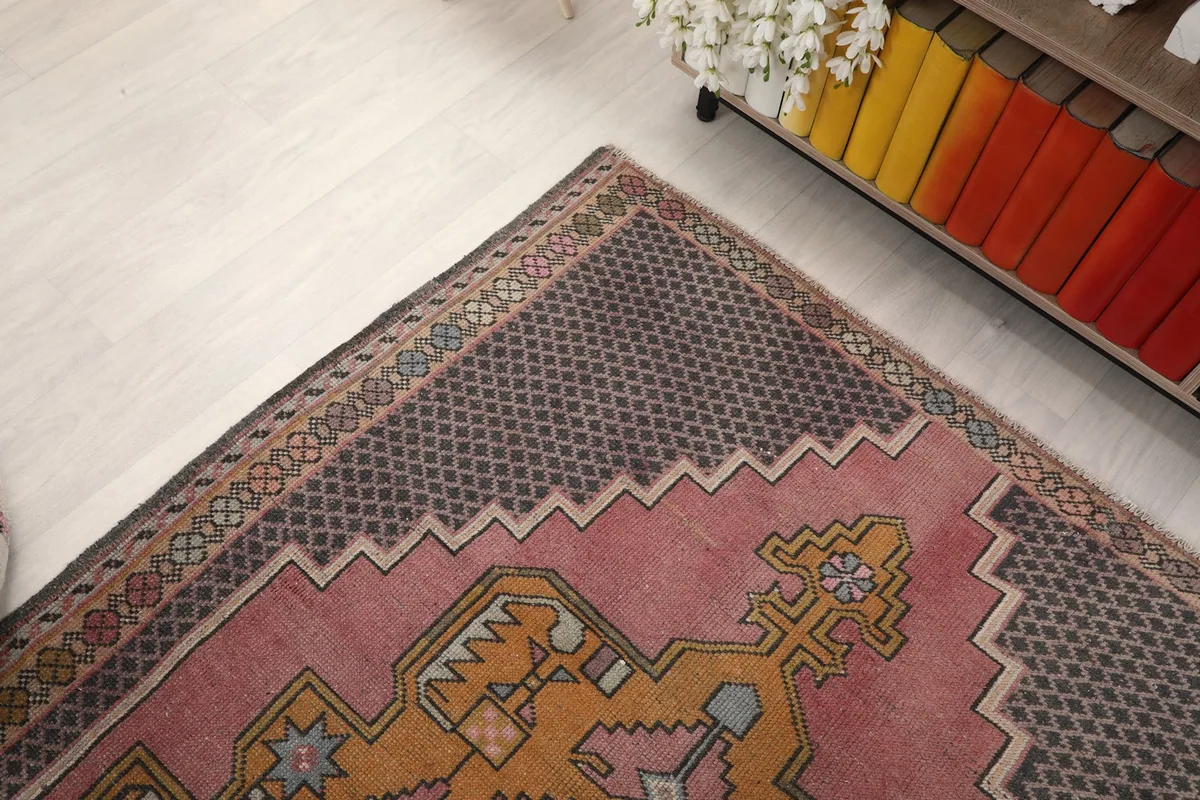 Corner view of the rug showing the charcoal border and part of the rose field next to a cabinet