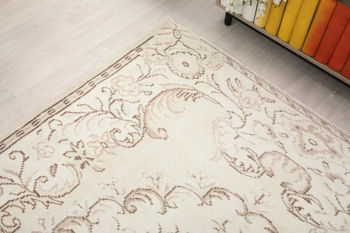Angle shot of the rug's surface, focusing on the intricate tan floral and vine motifs near the border