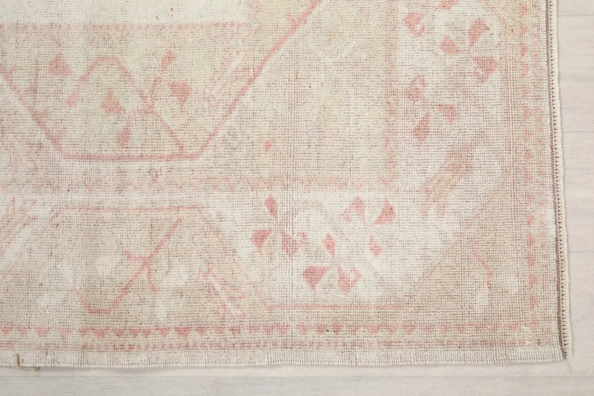 Detailed view of the border and faded geometric patterns in rose on a cream field