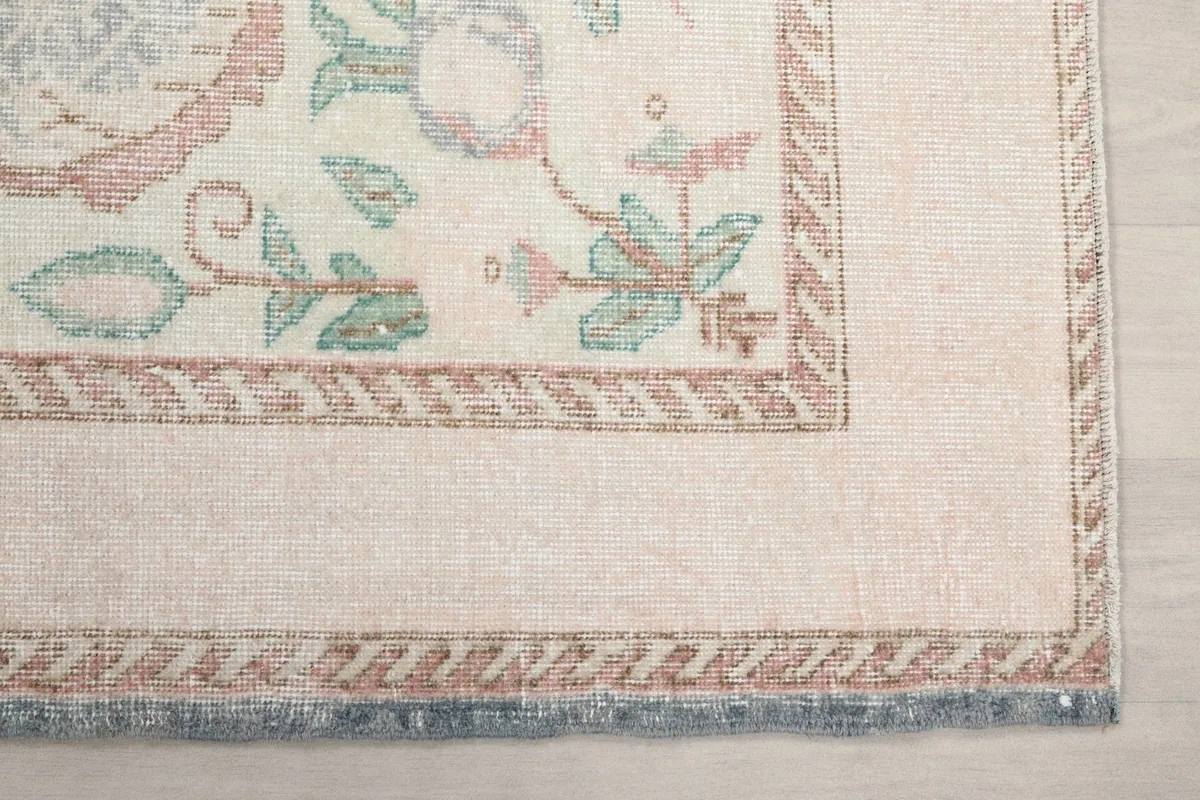 Detail of the rug's ivory border with a patterned edge and subtle rose and green motifs