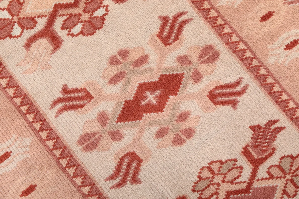 Close-up of the hand-knotted wool pile and a central tribal motif in cream and rose