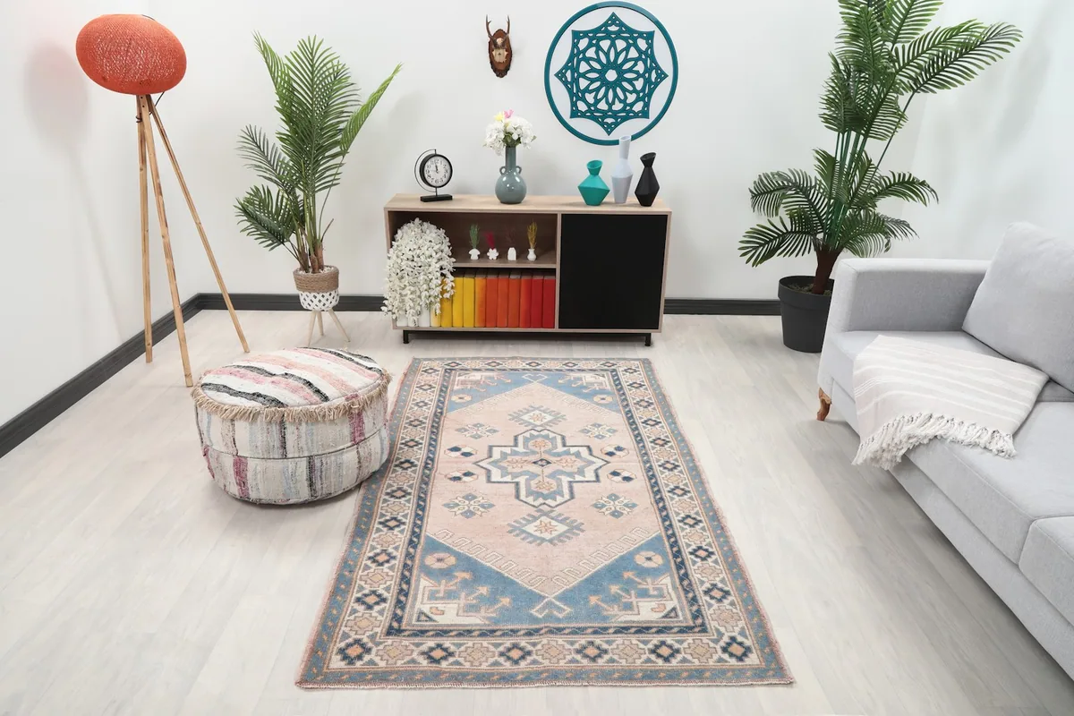 Vintage pink and blue rug placed in a modern living room setting with a gray sofa and wooden furniture.