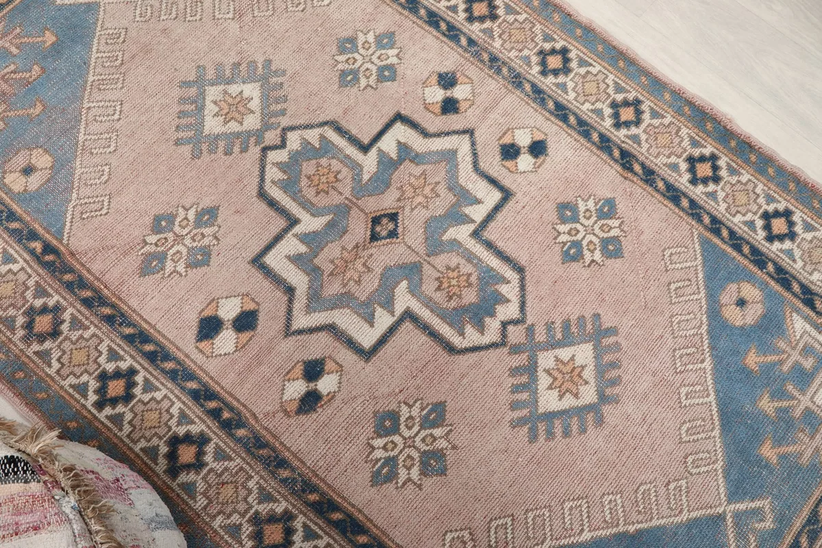 Close-up of the rug's central design, showing the pink field and intricate blue and beige geometric shapes.