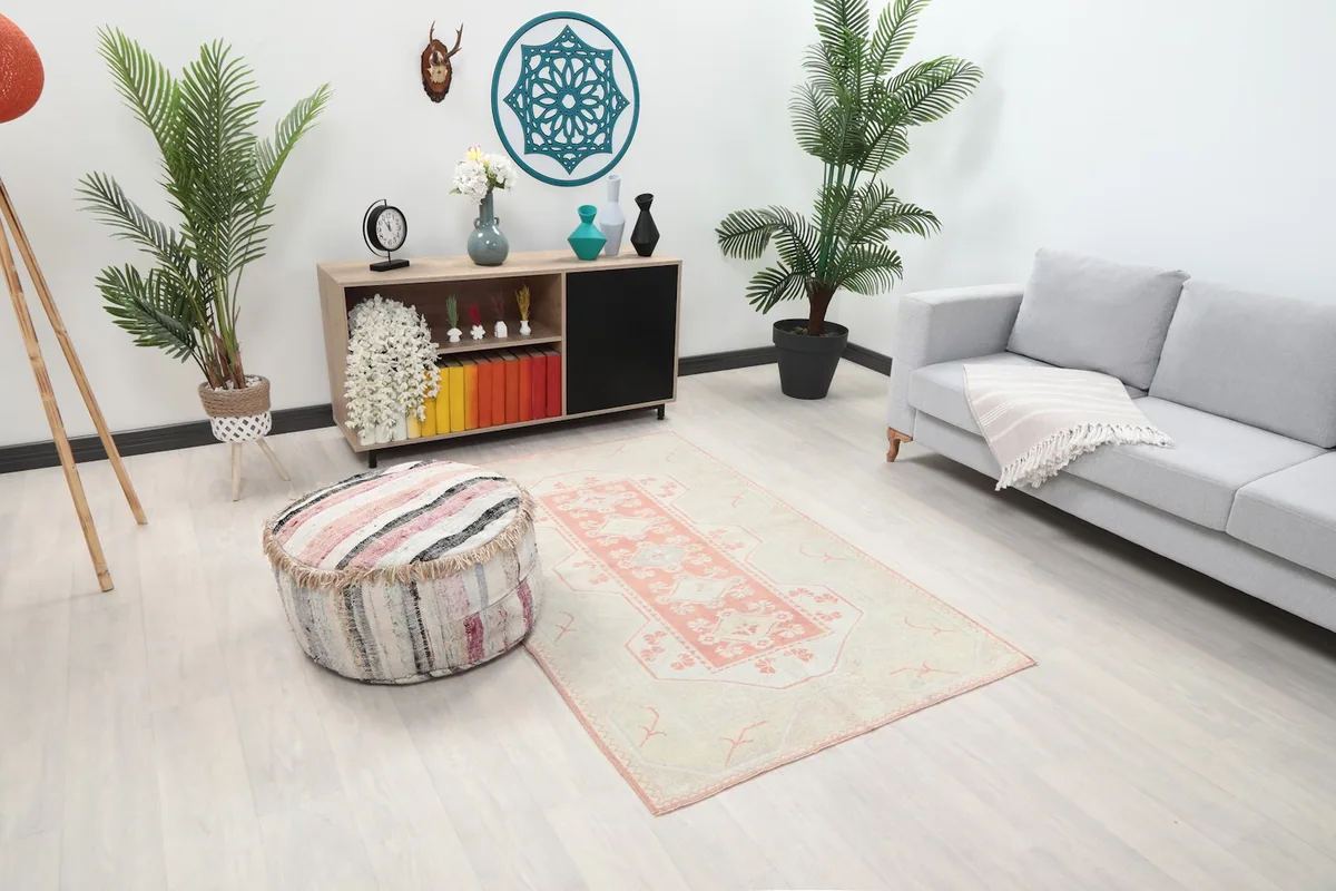 Angle view of the cream and pink rug in a room with a gray sofa and plants