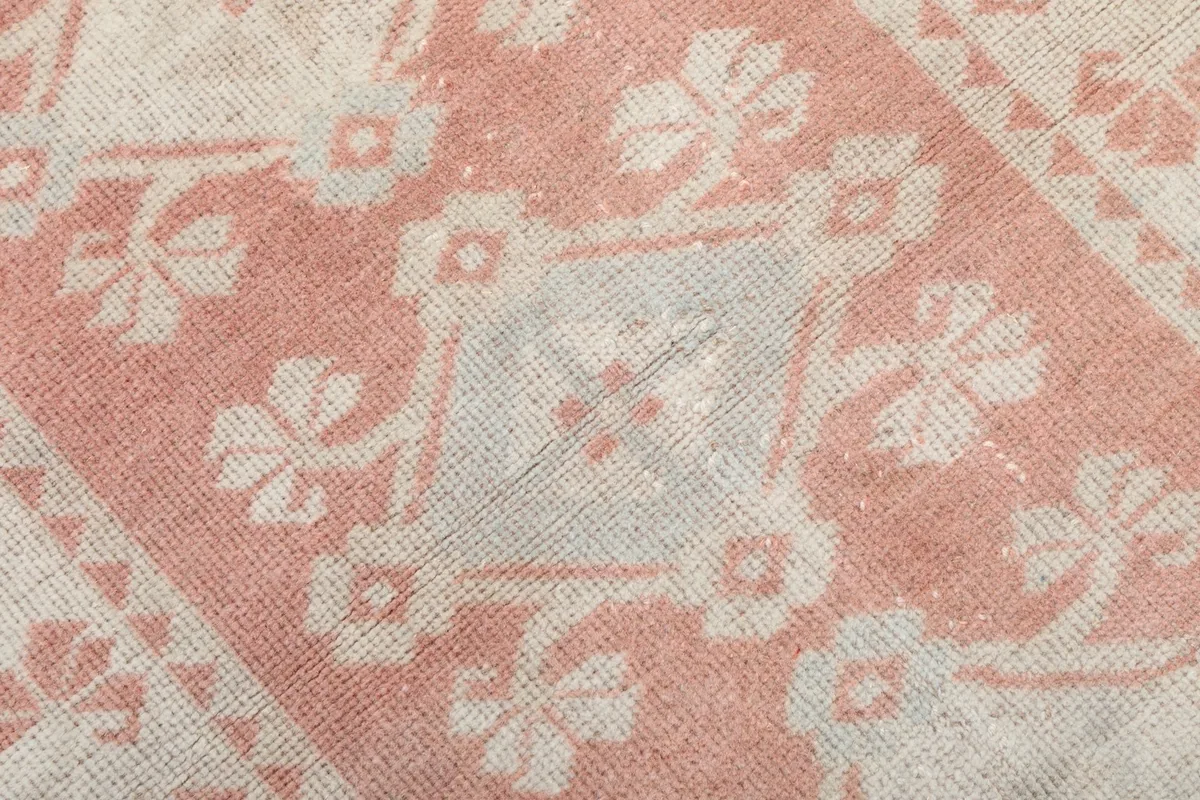 Extreme close-up of the hand-knotted wool pile showing pink and cream colors