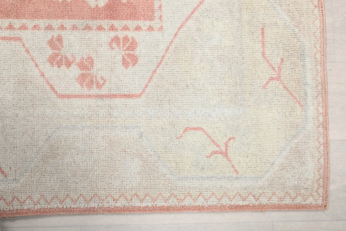Detail of the rug's cream border with pink accents and subtle geometric patterns