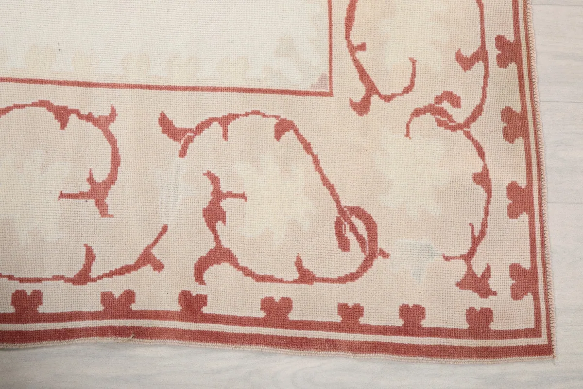 Close-up detail of the rose colored stylized floral motifs within the rug's border.