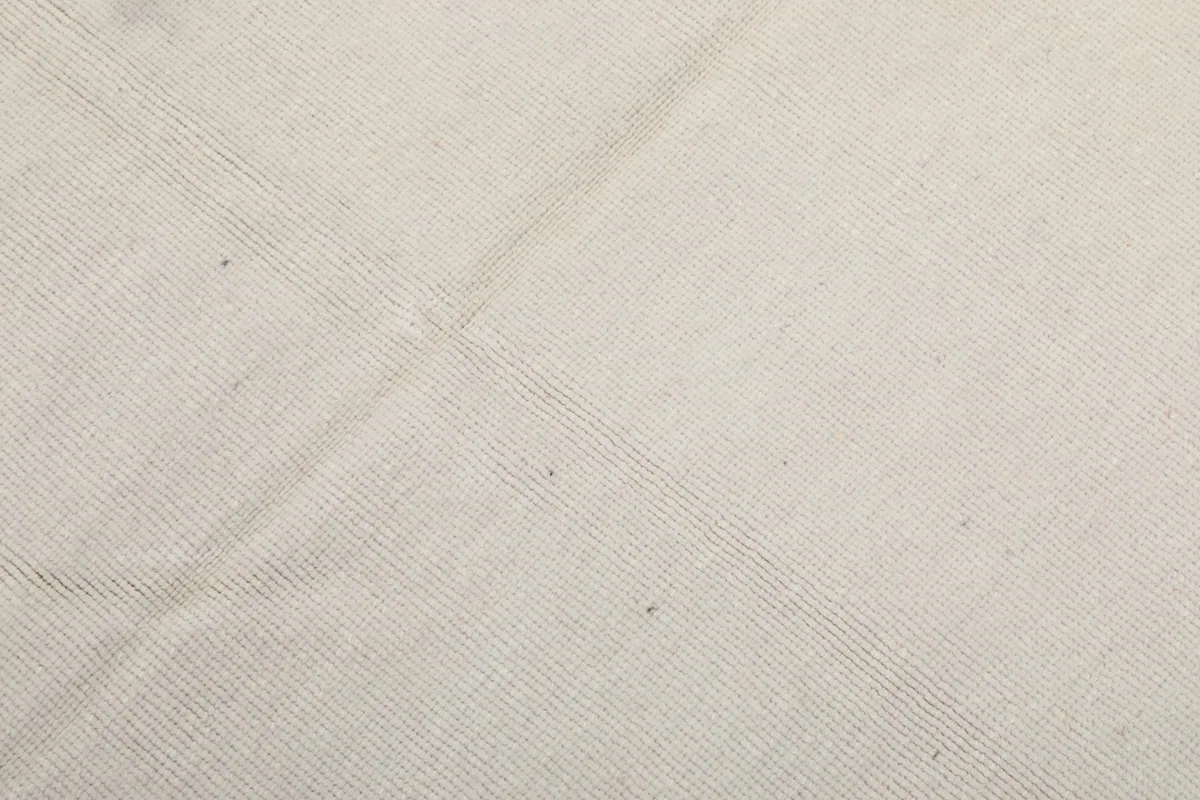 Close-up of the low wool pile texture on the ivory field of the vintage rug.