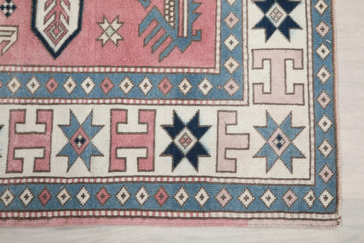 Detail of the rug's border with blue, ivory, and rose geometric motifs and stars