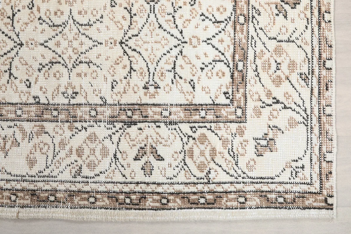Detailed view of the rug's corner, highlighting the intricate floral border in brown and tan