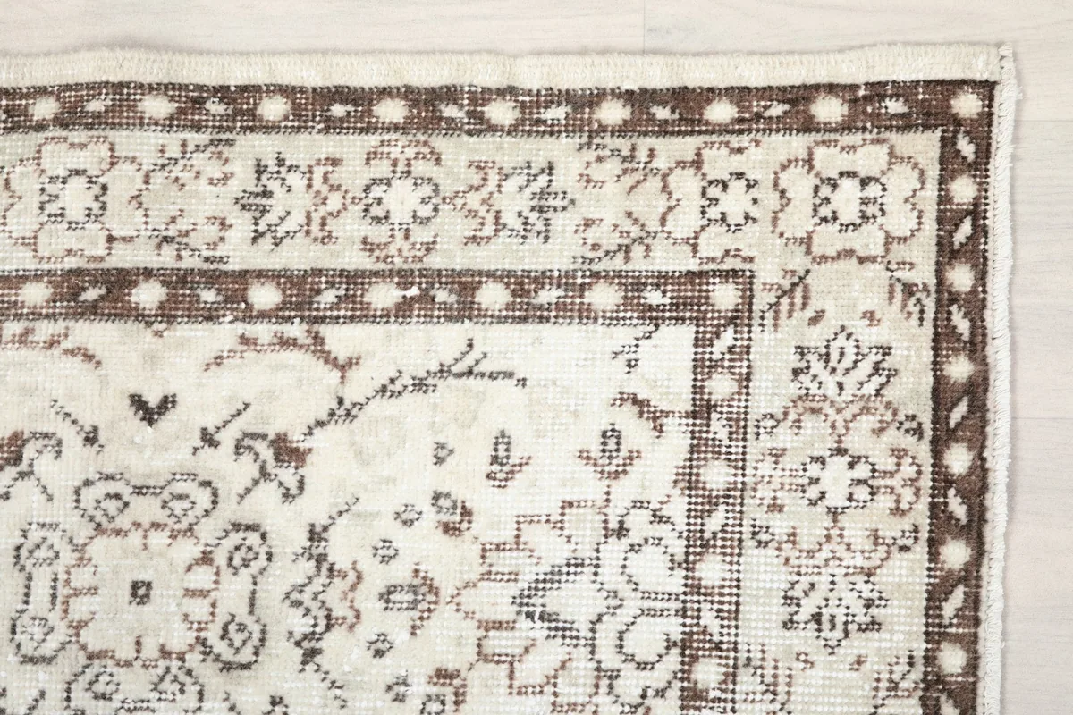 Detail of the rug's corner, showcasing the intricate brown border design against the ivory field.