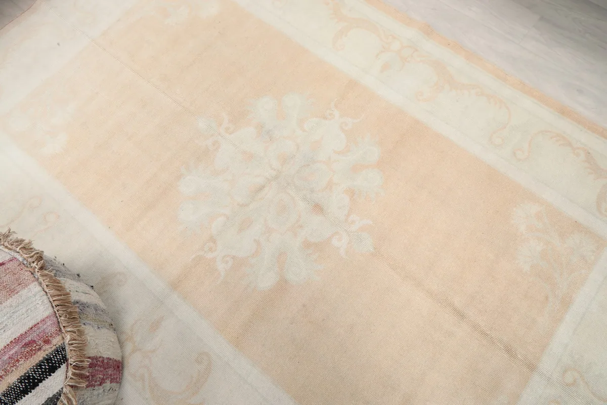 Overhead view focusing on the central ivory medallion and the beige field of the rug