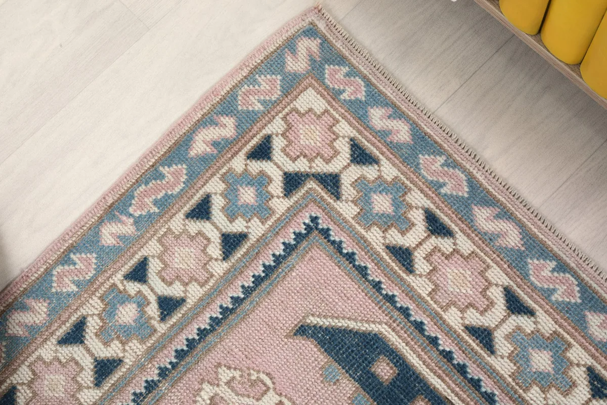 Angled close-up of a rug corner, showcasing the border details and the blend of pink and blue tones