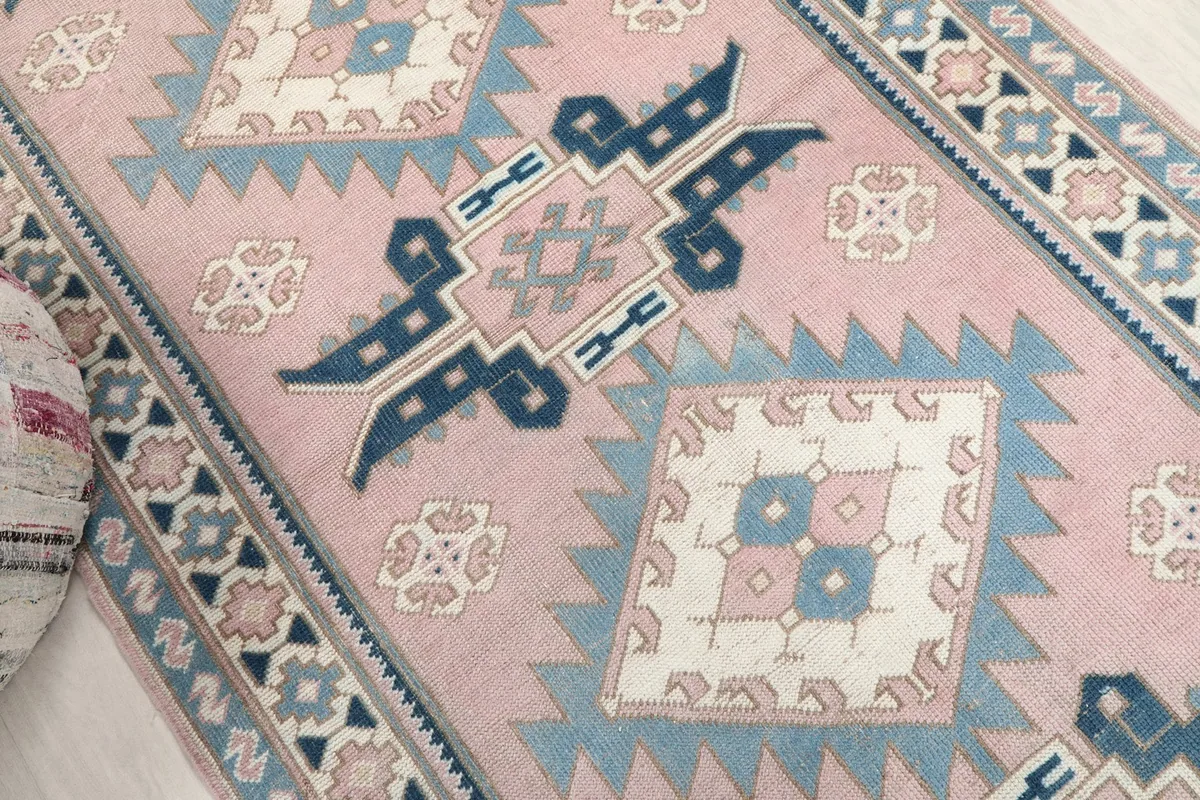 Overhead close-up of the rug's central geometric motifs in pink, blue, and ivory